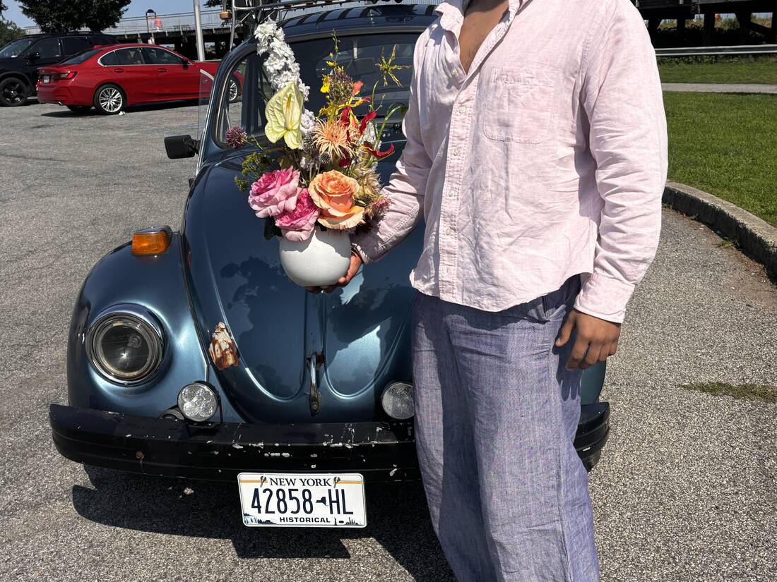 Arrangement of roses and anthurium held before a blue vintage Beetle